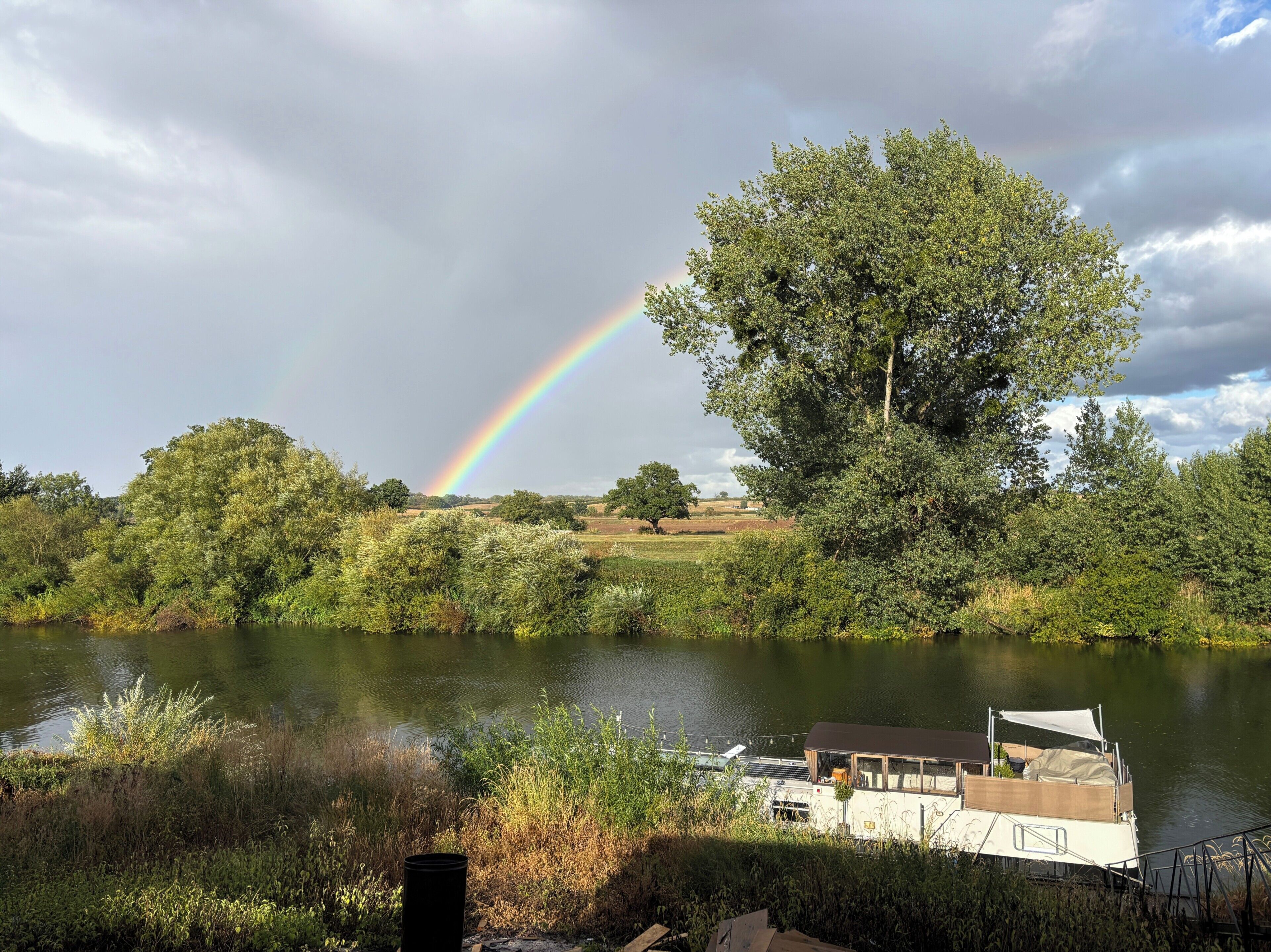 Een boot afgemeerd aan een kalm meer, met een regenboog op de achtergrond.