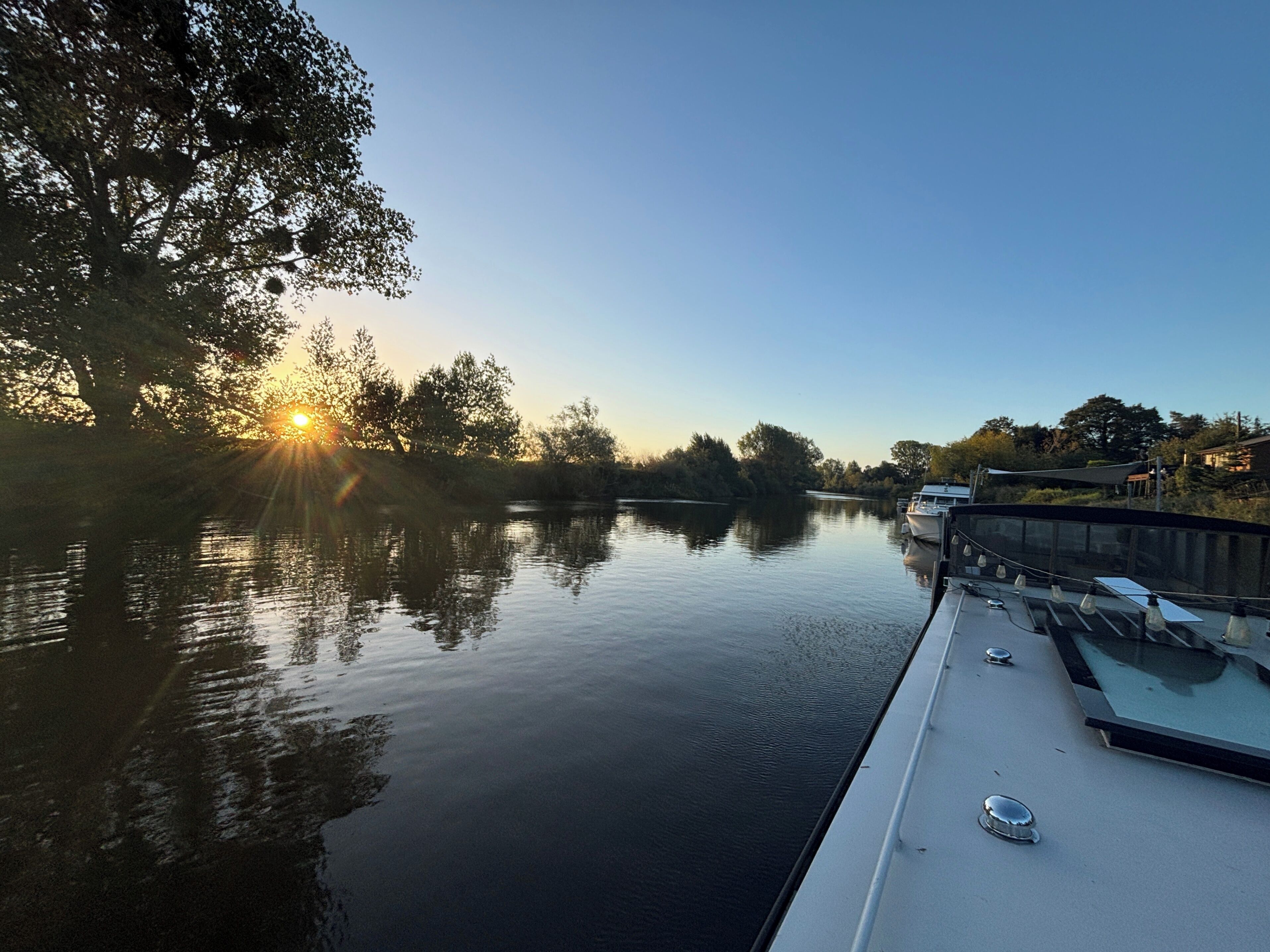 Ein ruhiger Fluss mit einem Boot, das an der rechten Seite anlegt, umgeben von Bäumen und einem klaren Himmel.
