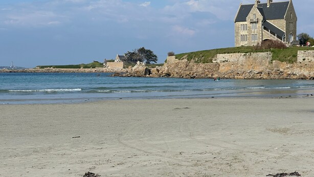 A coastal property with a large stone building, a beach, and a rocky shoreline.