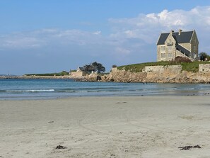 A coastal property with a large stone building, a beach, and a rocky shoreline.