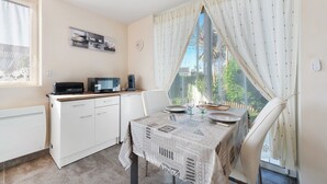 A kitchen with a dining table, chairs, a microwave, and a window with curtains.