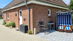 A brick building with a tiled roof, a small outdoor seating area with a table and chairs, and a blue-striped outdoor bench. - Apartment 'FeWo1' with Private Terrace and Wi-Fi (Oesterdeichstrich)