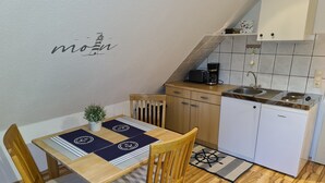 A compact kitchen with a dining area, wooden furniture, a small potted plant, and a wall decal. - Apartment 'FeWo1' with Private Terrace and Wi-Fi (Oesterdeichstrich)