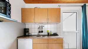 A compact kitchen with wooden cabinets, a sink, a coffee maker, and a refrigerator. - Apartment 'FeWo2' with Wi-Fi (Oesterdeichstrich)
