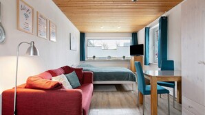 A modern room with a wooden ceiling, a bed, a desk with a chair, a red sofa, and a TV. - Apartment 'FeWo2' with Wi-Fi (Oesterdeichstrich)