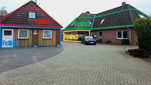 A row of three buildings with distinct roof colors and signage indicating 'FeWo1,' 'FeWo2,' and 'FeWo3.' - Apartment 'FeWo2' with Wi-Fi (Oesterdeichstrich)