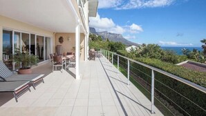 Un balcón con mobiliario exterior, vista al océano y una montaña de fondo.