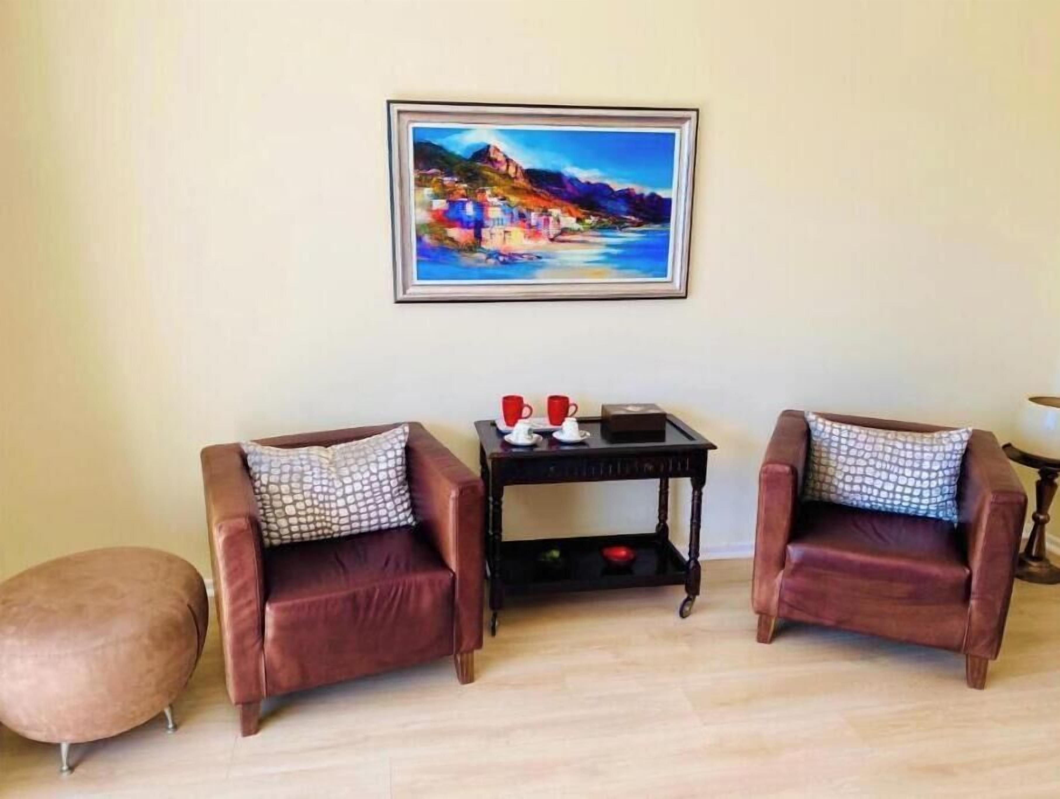 Een kamer met twee leren fauteuils, een klein tafeltje met een rode kop en schotel, en een lijst met een schilderij van een kustlandschap.