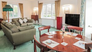 A living room with a sofa, a dining table with placemats, a television, and a window with curtains. - The Flat House (Taunton)