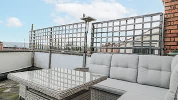 A rooftop terrace with a wicker table and grey cushioned seating.