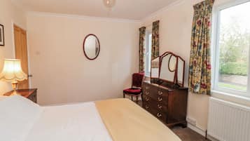 A bedroom with a bed, a dresser with a mirror, a chair, a lamp, and a window with curtains.