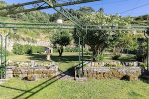 A stone pathway leading through a garden with a metal gate and a stone wall. - CDC Casa do Capitán Leiro: Relax Among Vineyards and Forests in Ribeiro (Cubilledo)