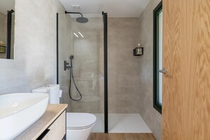 Un baño moderno con ducha de vidrio, inodoro blanco y tocador de madera.