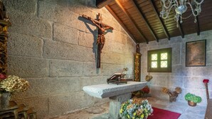 A stone wall with a crucifix, a wooden bench, and a chandelier. - CDC Casa do Capitán Leiro: Relax Among Vineyards and Forests in Ribeiro (Cubilledo)
