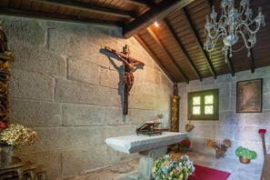 A stone wall with a crucifix, a wooden bench, and a chandelier. - CDC Casa do Capitán Leiro: Relax Among Vineyards and Forests in Ribeiro (Cubilledo)