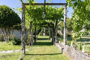 A garden pathway with a pergola structure, stone walls, and greenery. - CDC Casa do Capitán Leiro: Relax Among Vineyards and Forests in Ribeiro (Cubilledo)