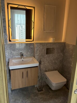 A compact bathroom with a sink, mirror, toilet, and shower. - ALSAWAH Iconic 3BR Apartment - ZED Towers (second alsheikh zayed)