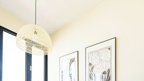 Zona pranzo con un tavolo lungo, sottopiatti intrecciati, sedie moderne, un lampadario e quadri appesi al muro.