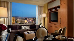 A hotel room with a large window offering a city view, a television, a sofa, a dining area, and a side table with a tray set. - 1-Bedroom / 1BB / Suite at Trump International Hotel Las Vegas - F1 Weekend!!! (Las Vegas)