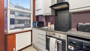 Uma cozinha compacta com micro-ondas, forno e máquina de lavar louça. Uma janela oferece vista para o exterior.