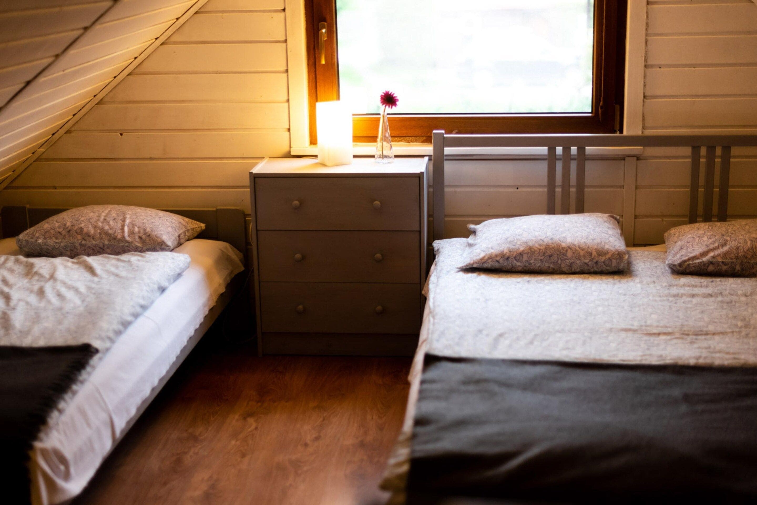 Un dormitorio con dos camas individuales, una mesita de noche con lámpara y una ventana con vistas a zonas verdes.