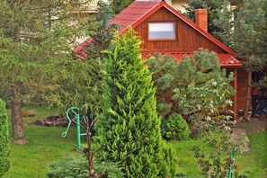 A wooden cabin with a red roof, surrounded by dense greenery and a garden. - Holiday Home With a Fireplace and a Large Terrace (Choczewo)