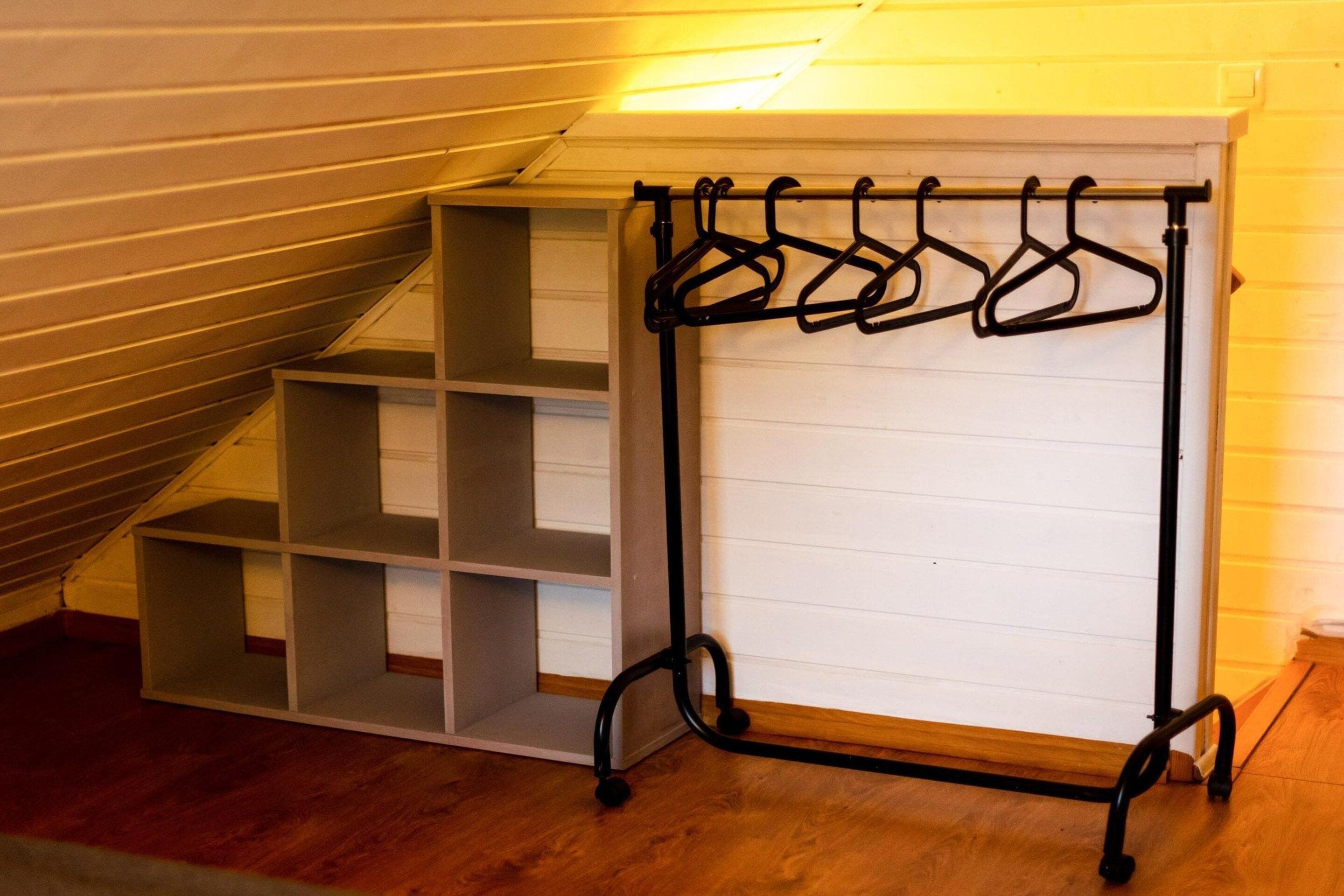 A room with a wooden floor, a white wall, and a black metal coat rack with multiple hooks.