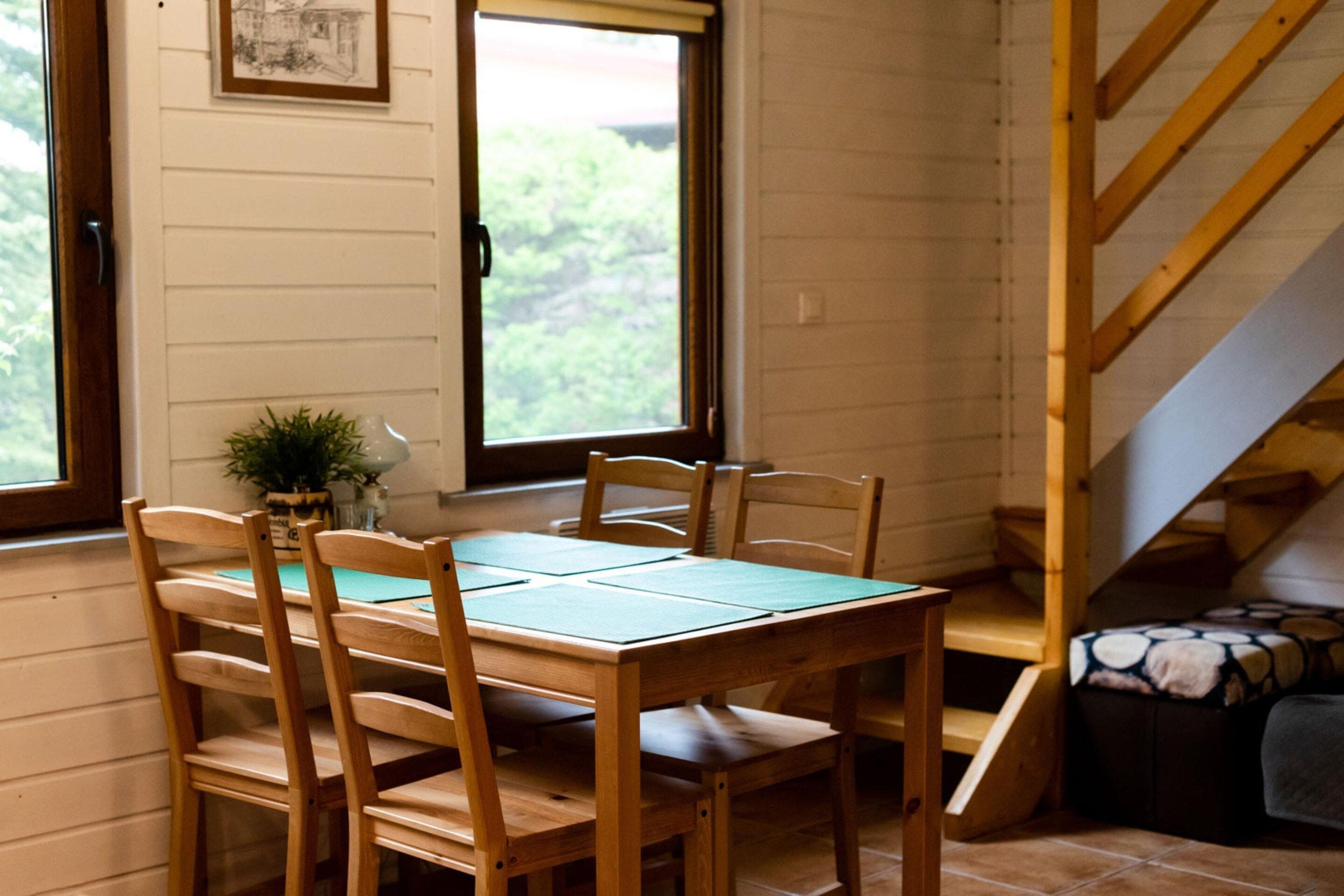 Una mesa de madera con sillas, una ventana con vistas a la vegetación y una escalera.
