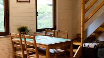Una mesa de madera con sillas, una ventana con vistas a la vegetación y una escalera.
