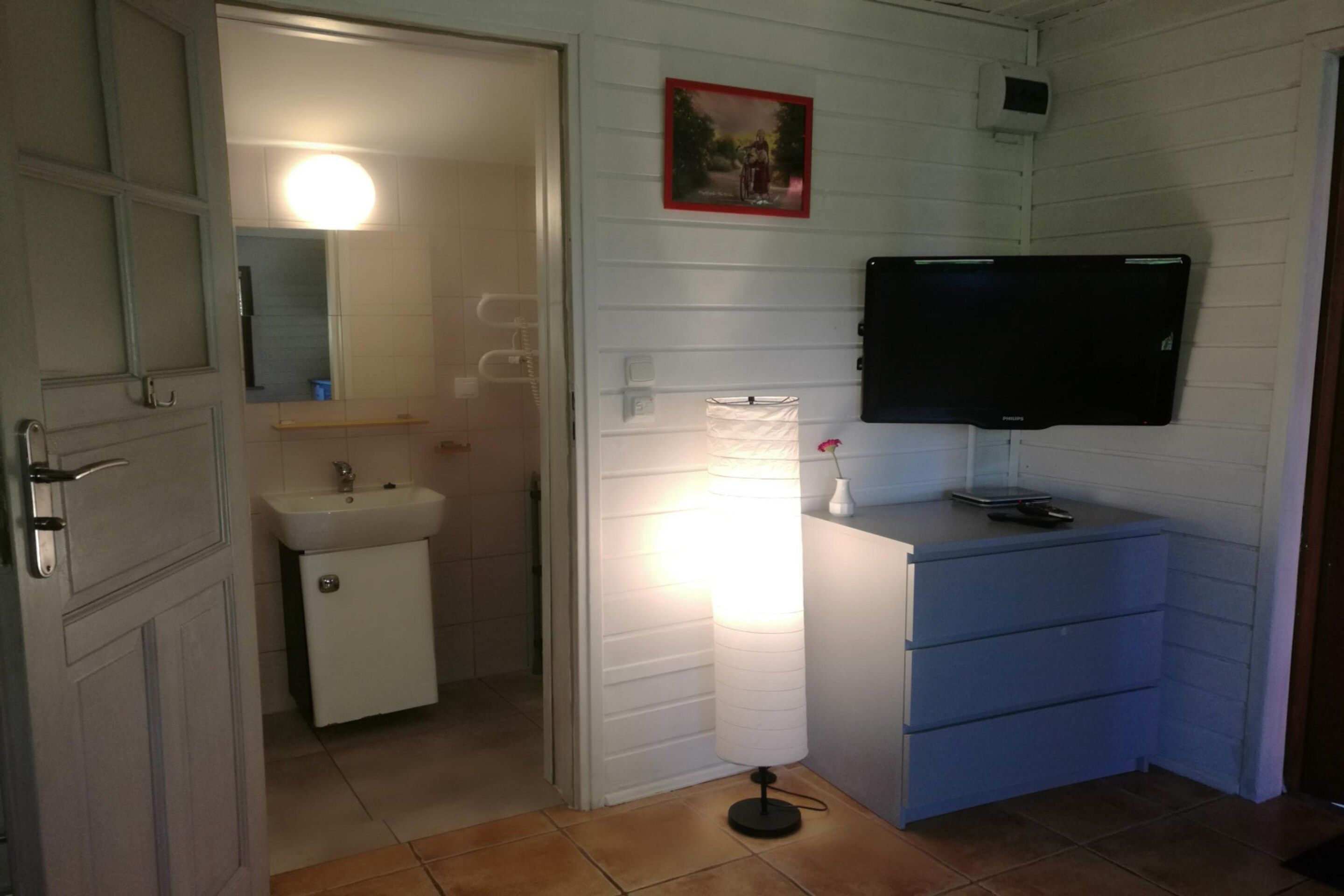 Ein Badezimmer mit Waschbecken, Spiegel und einem an der Wand befestigten Fernseher.