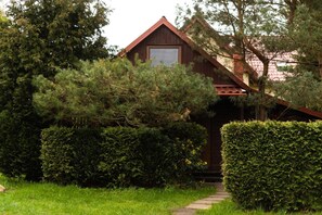 A wooden cabin with a sloped roof, surrounded by dense greenery and a well-maintained hedge. - Holiday Home With a Fireplace and a Large Terrace (Choczewo)
