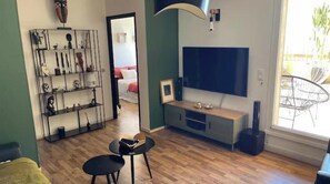A living room with a TV, a bookshelf, a small table, and a window with a view. - 2-bedroom family apartment with large terrace and sea view (Bastia)