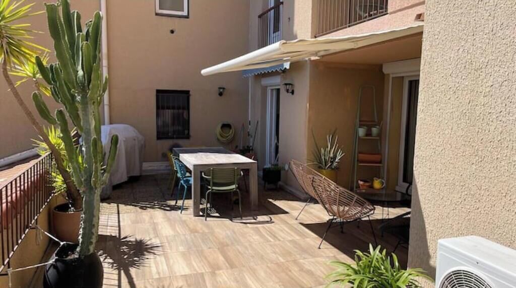 Un patio con mesa y sillas, una zona cubierta y plantas en macetas.