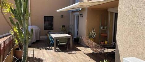 Un patio con mesa y sillas, una zona cubierta y plantas en macetas.