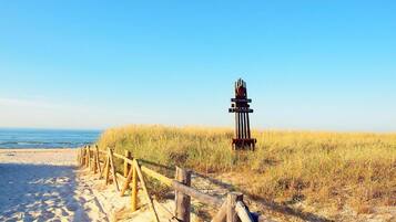 A sandy beach with a wooden fence leading to a structure with vertical poles and a circular top.