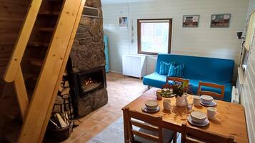 A cozy living room with a stone fireplace, a blue sofa, and a dining table set for four.