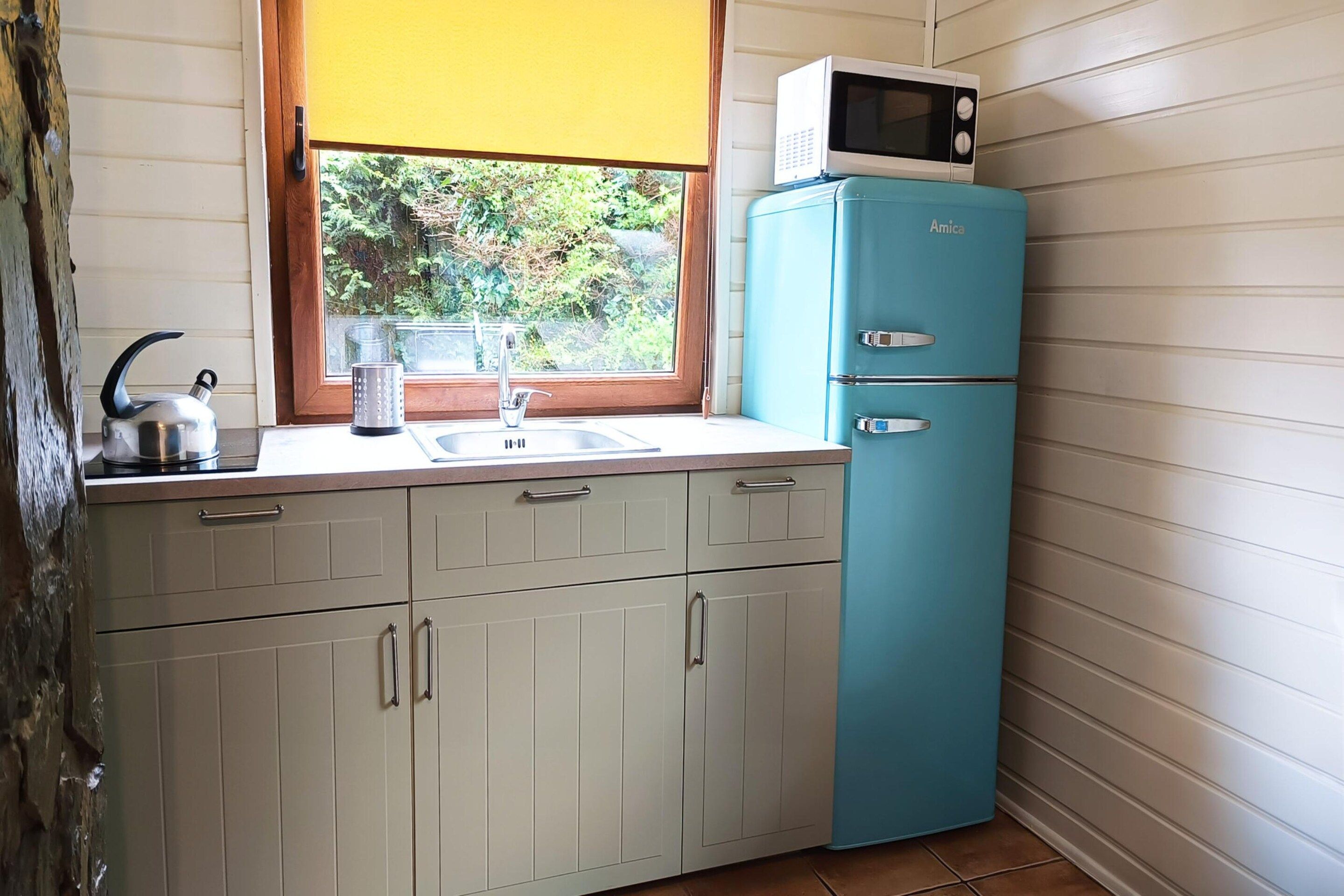 A compact kitchen with a sink, a kettle, a microwave, and a two-door refrigerator.