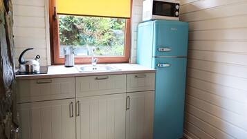 A compact kitchen with a sink, a kettle, a microwave, and a two-door refrigerator.
