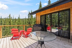 A deck with a glass table and red chairs, overlooking a forested area. - Luxury Breck Gem | Chefs Kitchen + Great Views (Breckenridge)