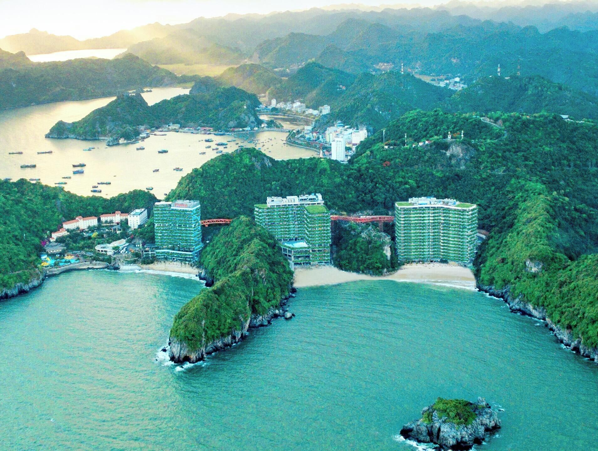 Una zona costera con varios edificios altos, una bahía con barcos y abundante vegetación.