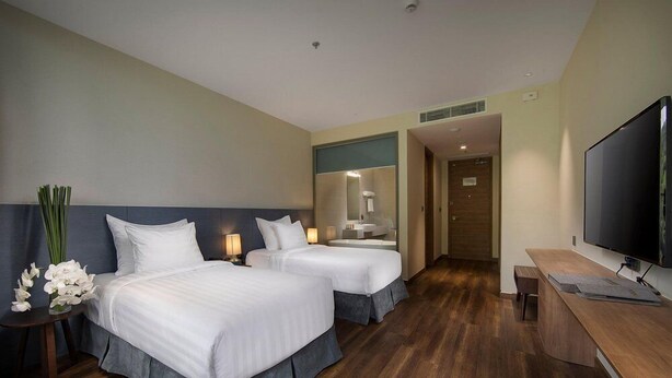 A hotel room with two beds, a desk, a TV, and a bathroom visible through an open door.