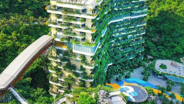 A multi-story hotel with balconies, a swimming pool, and a bridge.