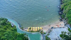 A coastal area with a beach, a swimming pool, and lush greenery.