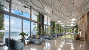 A modern hotel lobby with large windows, seating areas, and a view of the sea.