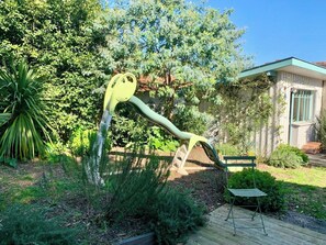 Un jardin agrémenté d’une sculpture originale, d’une terrasse en bois et d’un bâtiment doté d’un toit végétalisé.