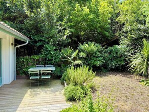 A wooden deck with a table and chairs, surrounded by dense greenery and a wooden fence. - Little idyll in the heart of Cap Ferret A0309 (Lège-Cap-Ferret)
