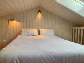 A bedroom with a sloped ceiling, a bed with white bedding, and a wall-mounted light fixture. - Little idyll in the heart of Cap Ferret A0309 (Lège-Cap-Ferret)