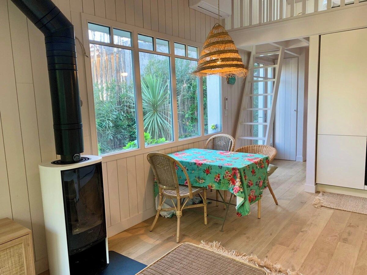 Une pièce avec une cheminée, une table à manger avec des chaises et une vue sur la verdure grâce à de grandes fenêtres.