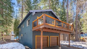 Eine zweistöckige Holzhütte mit Balkon, Garage und verschneitem Gelände.
