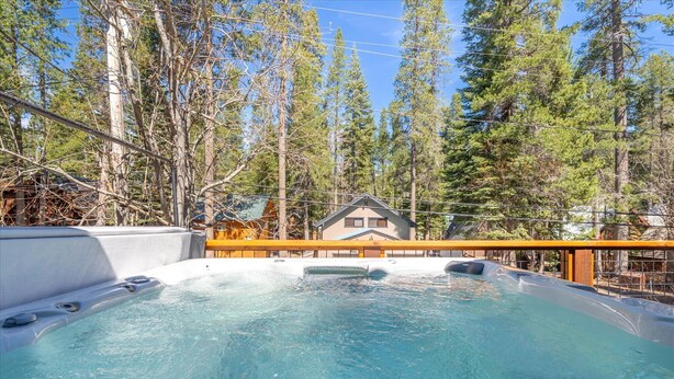 Ein Whirlpool, umgeben von hohen Bäumen, mit einer Holzterrasse und einem Haus im Hintergrund.